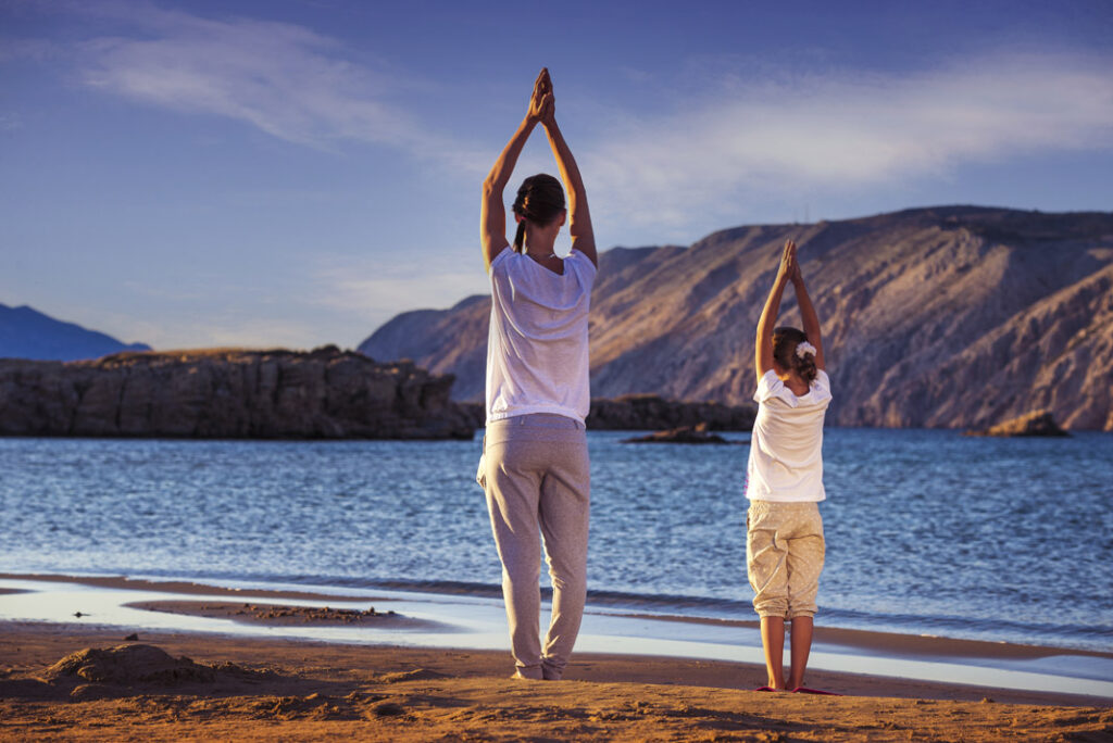 Mother and daughter, yoga on the beach early in the morning